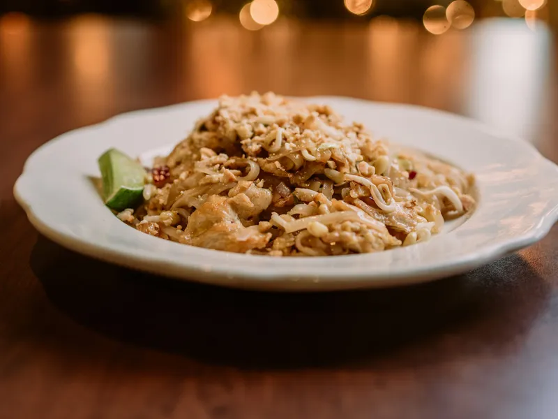 A plate of Pad Thai topped with ground peanuts and a lime wedge.