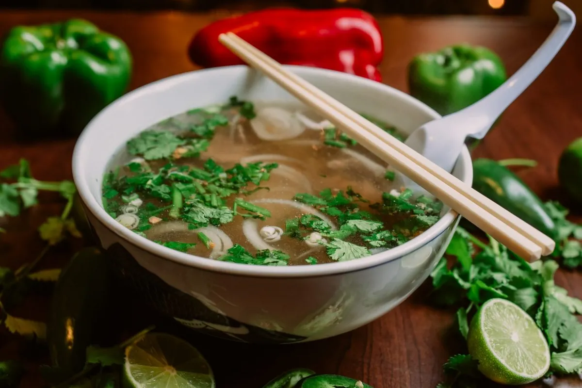 A bowl of pho with cilantro, onions and chopsticks resting on the rim.