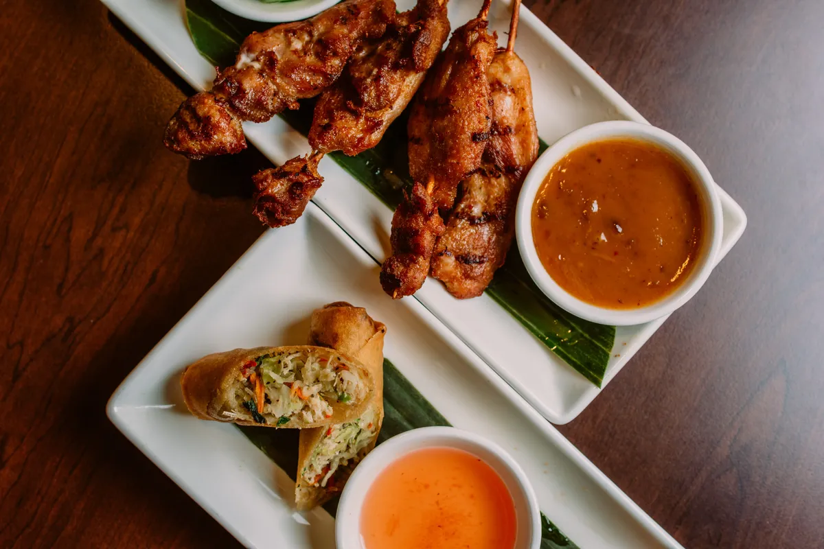 Chicken satay with peanut sauce beside Thai spring rolls with sweet and sour sauce.