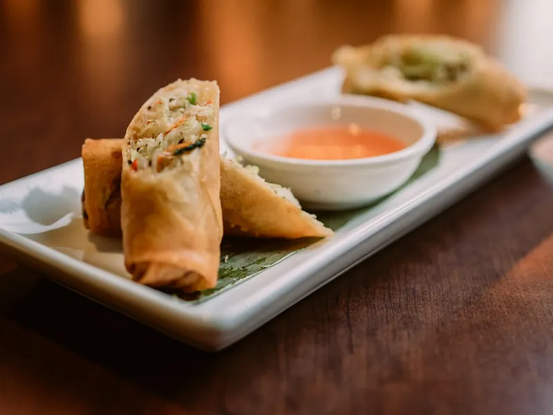 Golden Thai spring rolls cut open, served with sweet and sour sauce.